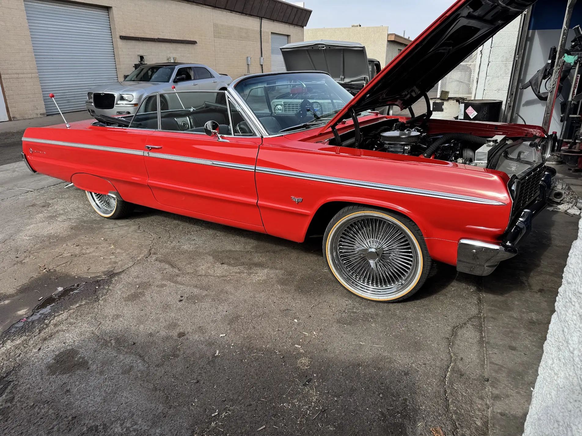 Red 1964 Chevrolet Impala convertible on chrome wire wheels in the SHM Motorsports shop