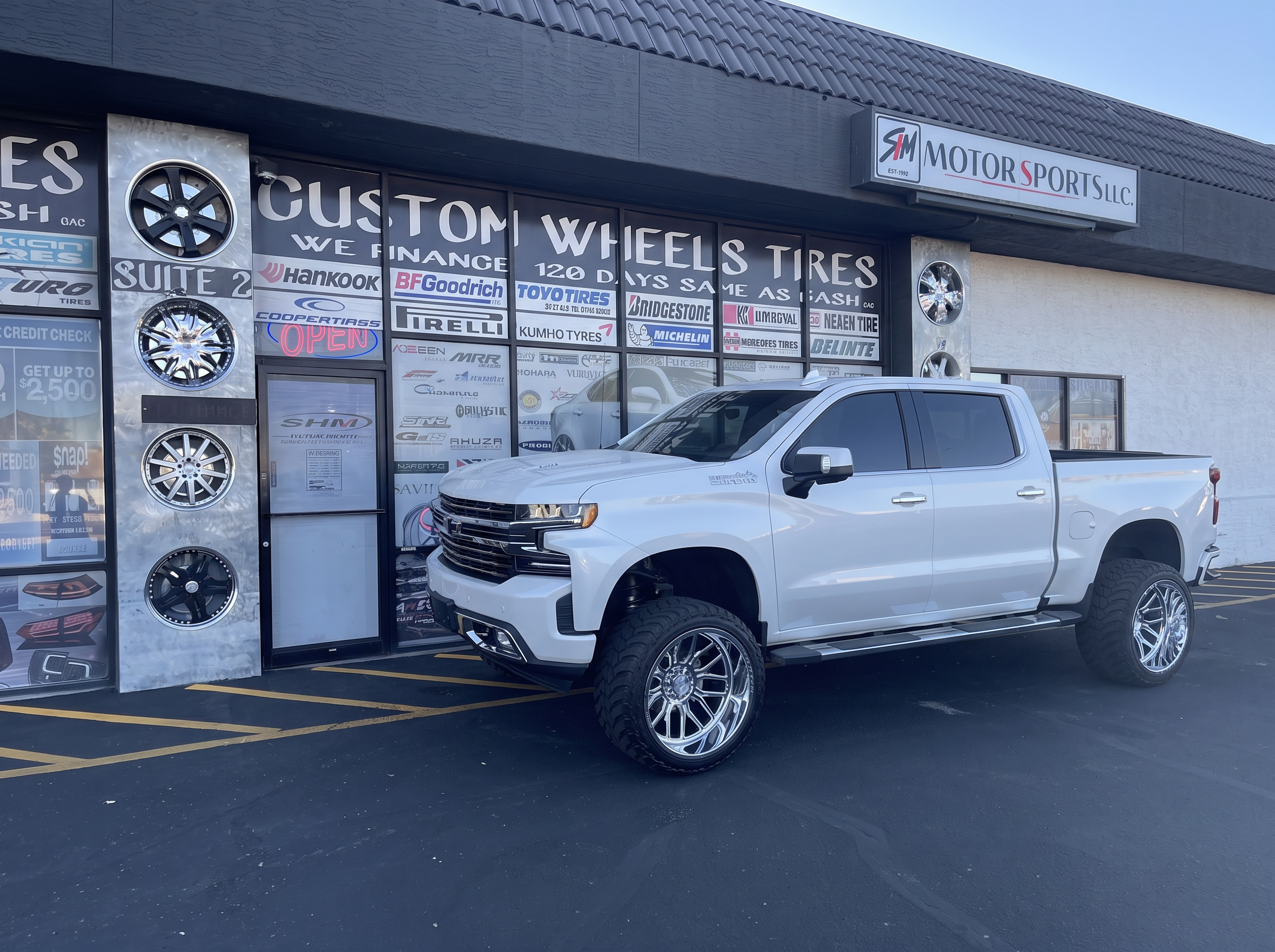 Front view of a lifted white 2021 Chevrolet Silverado High Country on 24x14 chrome AXE Wheels